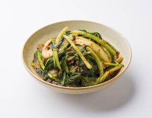 Wall Mural - Close-up of young radish kimchi with leaves and chili powder on dish and white floor, South Korea
