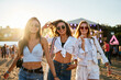 © artiemedvedev - Girls at beach music fest in summer. Friends laugh, dance in sun near sea. Young women enjoy festival atmosphere, wear trendy sunglasses, casual outfits. Partygoers celebrate outdoor event together.