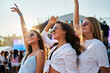 © artiemedvedev - Group of three young women enjoying summer music festival on sandy shore. Arms raised, dancing in evening light. Fashionable friends party, carefree atmosphere with ocean backdrop on warm day.