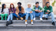 © Lomb - Diverse group of young friends using smartphones outdoors, multicultural millennials socializing, digital connectivity, urban lifestyle, inclusive friendship