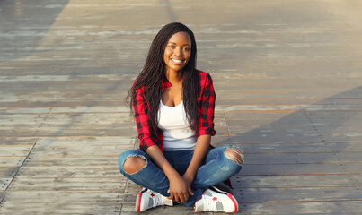 Wall Mural - Modern happy young african woman smiles sitting on the floor with dreadlocks, black girl in the city