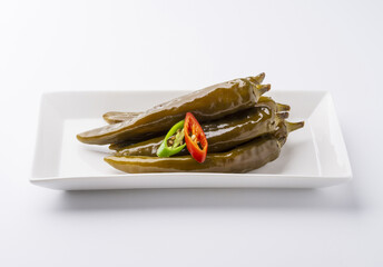 close-up of pickled chili peppers with red and green pepper pieces on rectangular dish and white flo