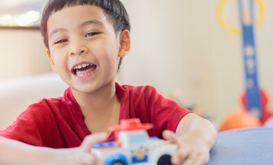 Portrait image of cheerful little Asian boy sitting and looking at camera while playing with toy cars