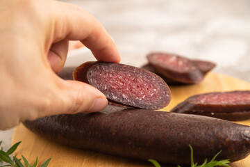 Sujuk sausage with hand on wooden cutting board with pepper and herbs on brown concrete. Side view, selective focus.