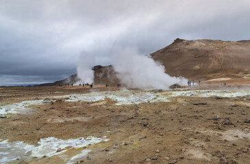 High angle and summer view of tourists on dirt ground besides vapor of geothermal spa at Hverir, Iceland
