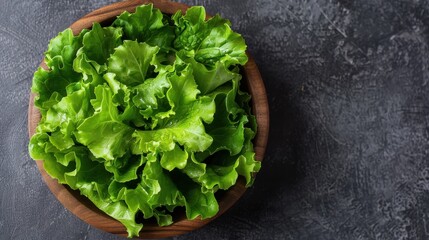 Wall Mural - A wooden bowl is filled with fresh and vibrant green leaf lettuce, a perfect representation of healthy, organic produce ready for consumption in salads or other healthy dishes.