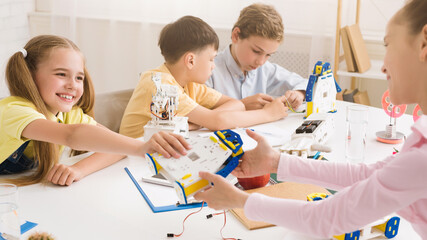 Aufkleber - Four students, three girls and one boy, work together to build a robot during a STEM class. The students are all smiling and engaged in the activity, demonstrating their interest in science