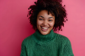 Wall Mural - Portrait of good looking curly ethnic woman smiles broadly, enjoys day off, has happy talk with interlocutor, discusses holiday preparation, wears green sweater, isolated on pink background.