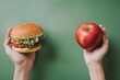 © Maryam - A vivid comparison of unhealthy and healthy food choices; a hamburger held in one hand and a fresh apple in the other against a green background