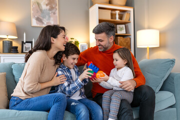 Poster - Cheerful son and daughter sitting with parents playing at home. Playful little boy and girl enjoying spending time with parents at home.