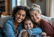© Bundi - Mom, grandmother, and child hug in a portrait for mothers day on a sofa in a Colombian house. Mama and elderly woman love hugging a young girl or child.