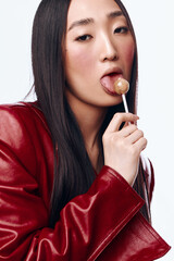 Wall Mural - Attractive woman with long black hair and a red jacket enjoying a sweet lollipop