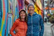 © CogniLens - Portrait of a grinning couple in their 30s showing off a lightweight base layer while standing against vibrant market street background