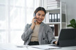 © amnaj - Businesswoman talking on phone and working on laptop in modern office, multitasking and professional atmosphere.