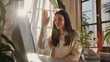 © VK Studio - A woman waves at her computer during a virtual meeting in a sunlit room, surrounded by plants, exuding warmth and productivity.