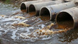 © sornram - Industrial wastewater flowing from large pipes into a polluted river, creating environmental contamination concerns.