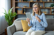 © Liubomir - An elderly woman engages in virtual consultation with psychologist, displaying frustration and concern while sitting on sofa at home. Concept includes mental health, online therapy