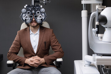 Portrait happy young man doing eye test on phoropter, male eyesight check with optometry machine