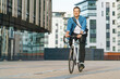 © muse studio - A smiling young man cycling through an urban area, surrounded by modern architecture and buildings.