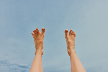 Person's legs up in air against blue sky with few clouds in background