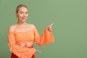 Wall Mural - Pretty young woman pointing at something on green background