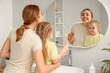 © Pixel-Shot - Young mother and her little daughter with toothbrushes near mirror in bathroom