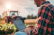 © ylivdesign - Modern agriculture concept with a farmer analyzing data on a laptop with a tractor in the background