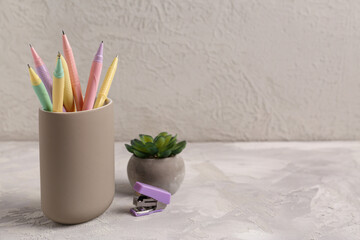 Wall Mural - Holder with pens, stapler and flowerpot on light background