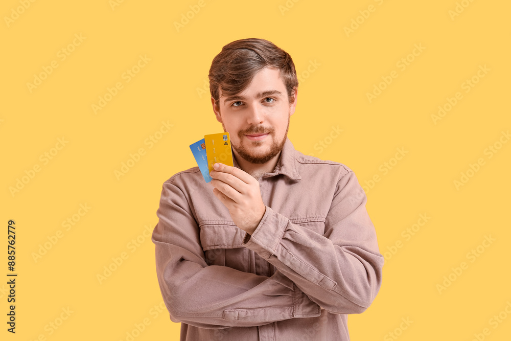 Young man with credit cards on yellow background