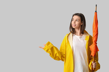 Wall Mural - Young happy woman in raincoat with umbrella on grey background