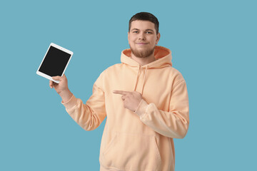 Canvas Print - Young bearded man pointing at tablet computer on blue background