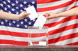 © Pixel-Shot - Voting women near ballot box on table against flag of USA