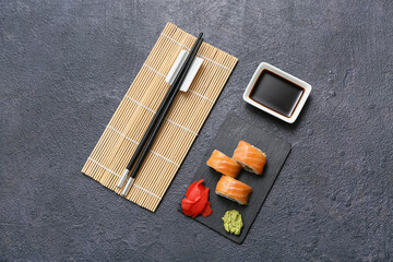 Wall Mural - Tasty sushi rolls with soy sauce, chopsticks and bamboo mat on black grunge background