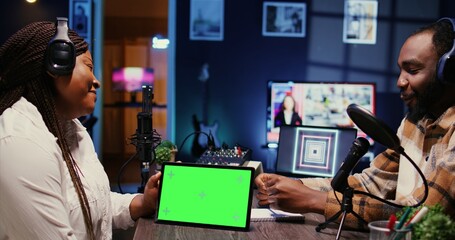 Wall Mural - Woman and man participating in podcast, laughing while watching funny internet clips on green screen tablet in studio, discussing content. Podcasters reacting to amusing videos on chroma key device