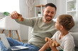 © Pixel-Shot - Little son and his father playing wooden toys while working with laptop at home