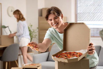 Canvas Print - Young man with piece of tasty pizza and his girlfriend in living room on moving day