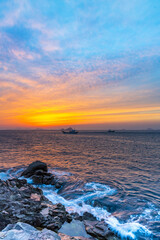 Sunset view of wave on seaside rocks with two fishing boats on the sea against glow in the sky at Somaemul Island near Tongyeong-si, South Korea
