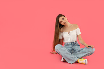 Wall Mural - Attractive young girl sits on a pink background