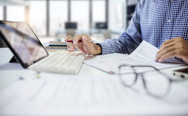 Wall Mural - Asian businessman using tablet with keyboard working and reviewing document report at office workplace. professional lawyer reading and checking financial documents or insurance contract