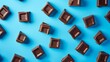 © Xyeppup - Aerial view of milk chocolate squares scattered on a vibrant blue background, creating a visually appealing contrast between the chocolate and the backdrop