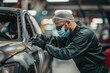 © ylivdesign - Car mechanic wearing protective mask carefully applying sealant to a car body in a workshop