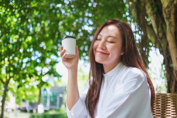 Wall Mural - Portrait image of a young woman with closed eyes holding and drinking coffee in the garden