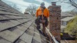 © INT888 - A roofer in safety gear works on a residential roof with a brick chimney.