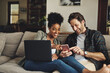 © aLListar/peopleimages.com - Couple, relax and happy with technology on sofa for social media, streaming subscription and online shopping for apartment. Man, woman and together in home with laptop or smartphone for connectivity.