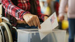 © Anastasiia Shkut - Close-up of a man in a wheelchair casting his ballot with the United States flag into the ballot box at an accessible voting station, USA presidential election
