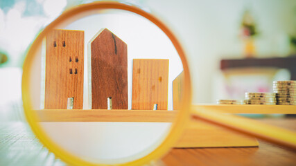 Wall Mural - Hand holding magnifying glass and looking at house model, house selection, real estate concept.