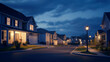 © Natalia - Peaceful suburban neighborhood at night with houses illuminated by streetlights and porch lights under a partly cloudy sky.