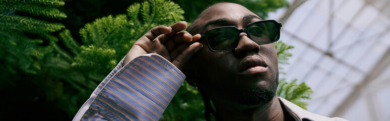 An African American man in sunglasses and sophisticated attire in a vibrant green garden.