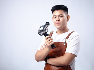 An Asian man in a brown apron and white shirt smiles while holding up a metal scraper, standing against a light grey studio background.