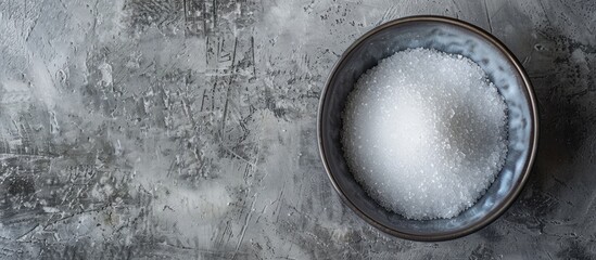 Poster - Top view of a bowl with granulated sugar on a textured grey table providing ample space for text in the image